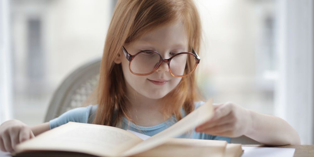 Meisje met bril leest geconcentreerd een boek